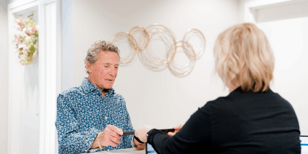 A patient at the front desk of Ohio Dental Implants & Oral Surgery handing over a tablet, representing the streamlined check-in and insurance processing at the office.